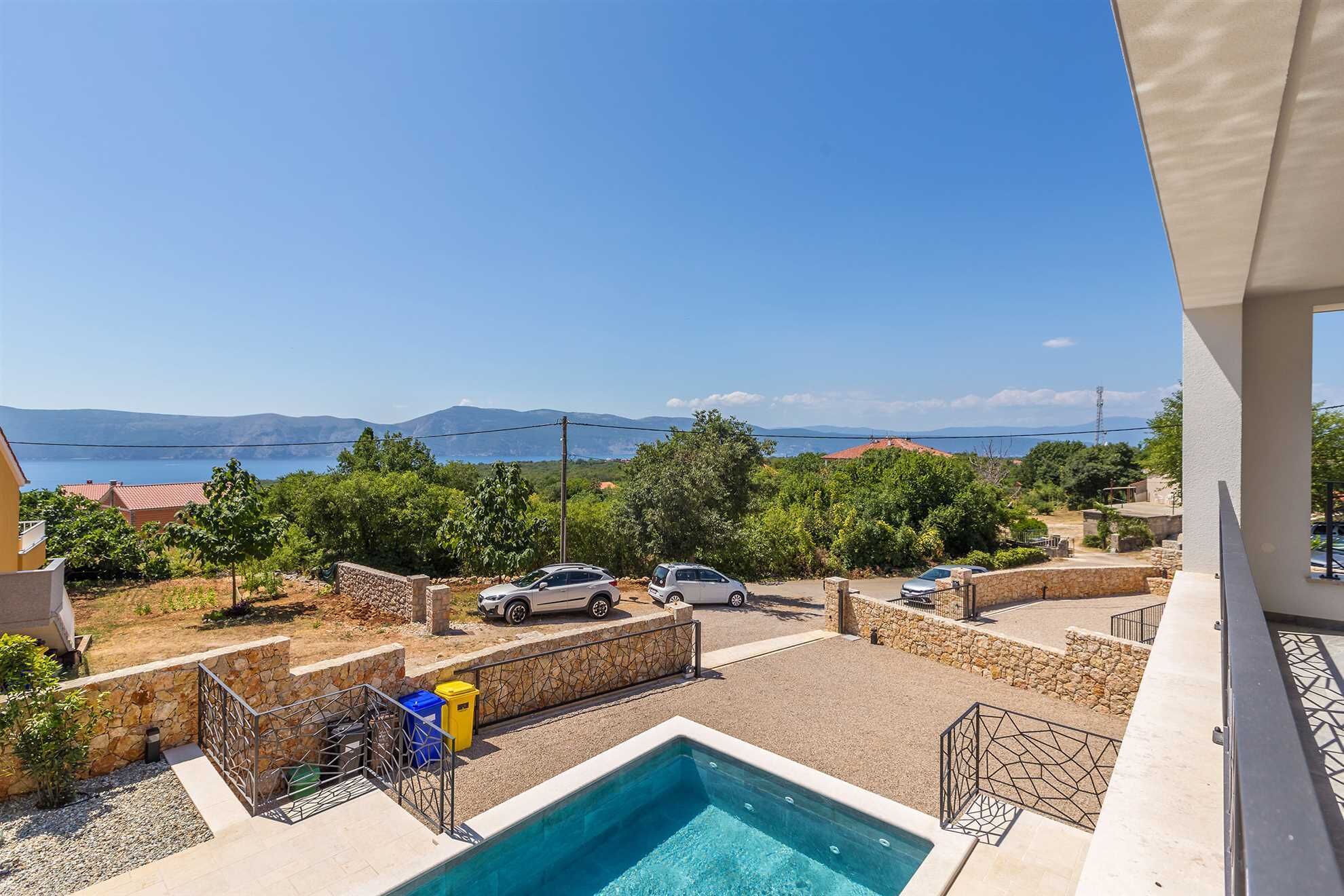 Uma área de piscina com vista para o mar e montanhas, ladeada por paredes de pedra e vegetação.