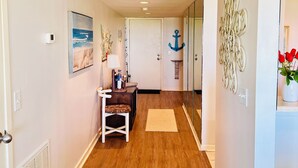 Un corridoio con pavimento in legno, una porta bianca, un piccolo tavolo con una lampada e un'ancora decorativa appesa al muro.