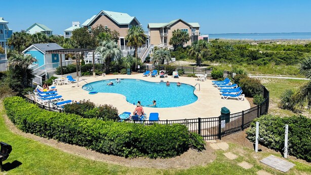 Un resort con piscina centrale circondata da lettini e un'area solarium recintata.
