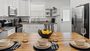 A modern kitchen with white cabinets, a stainless steel refrigerator, and a wooden dining table set for four. - Tampa Stylish Bungalow Oasis (Tampa)