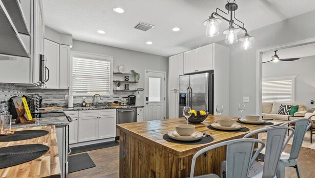A modern kitchen with white cabinets, a wooden island, and a dining area with a table and chairs. - Tampa Stylish Bungalow Oasis (Tampa)