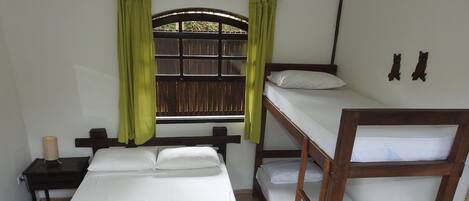 A room with a bunk bed, a single bed, a nightstand, a lamp, and a window with curtains.