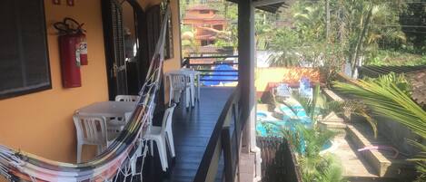 A covered outdoor area with a hammock, white plastic chairs, and a pool.