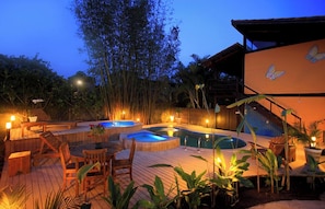 Una terraza de madera con jacuzzi, zona de estar y piscina.