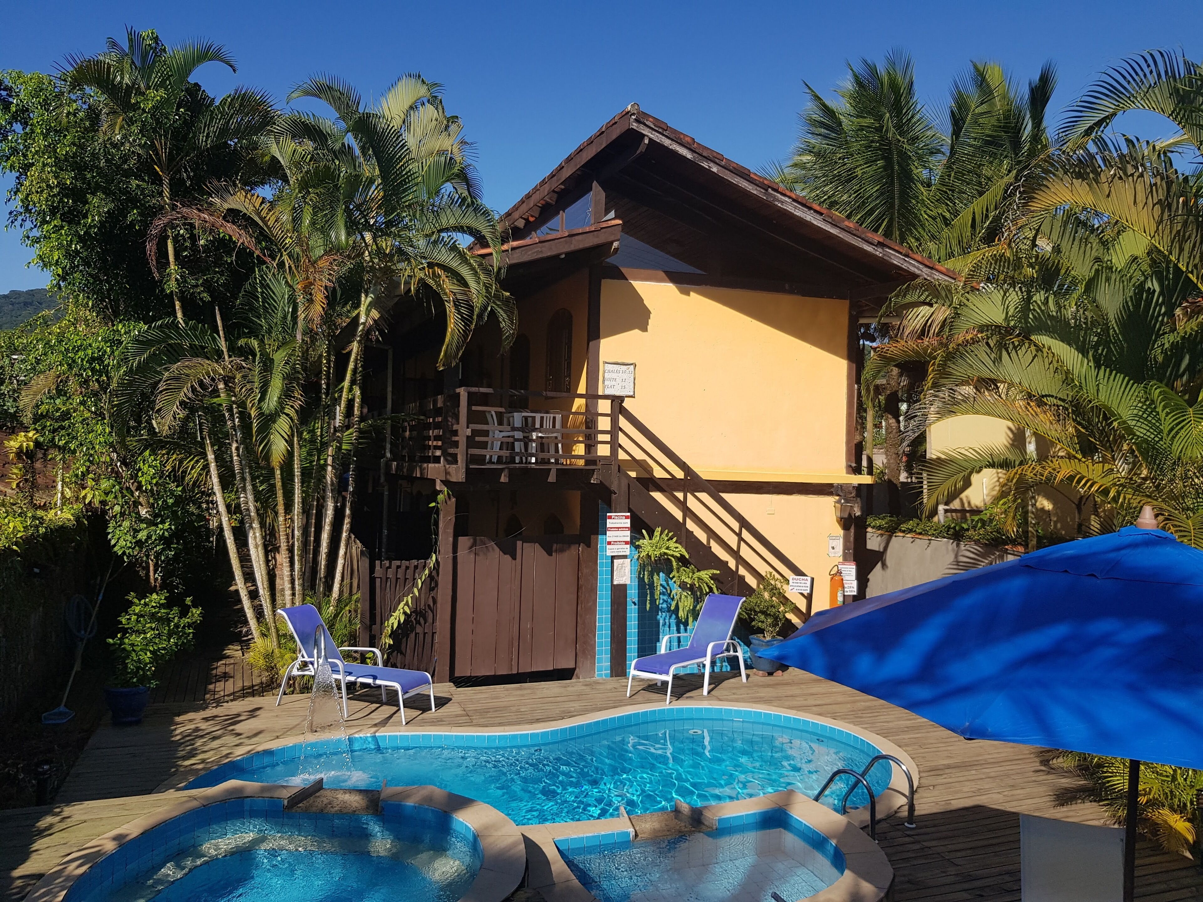 A hotel with a pool, lounge chairs, and tropical vegetation.