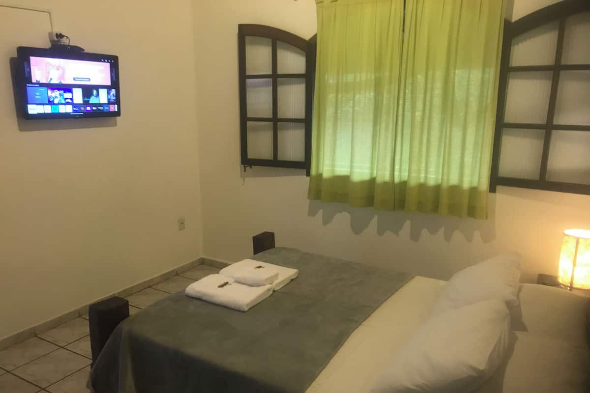Ein Hotelzimmer mit Bett, Tisch mit Handtüchern, Fernseher an der Wand und einem Fenster mit Vorhängen.