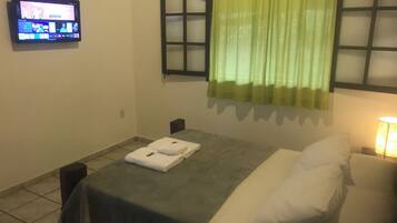 Habitación de hotel con cama, mesa con toallas, televisor en la pared y ventana con cortinas.