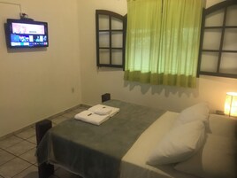 Een hotelkamer met een bed, een tafel met handdoeken, een televisie aan de muur en een raam met gordijnen.