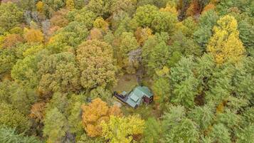 An aerial view of a forested area with a cabin featuring a green roof and a small porch.