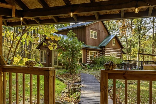 Une cabane en bois dotée d’un porche, d’un chemin menant à l’entrée et bordée par une forêt.