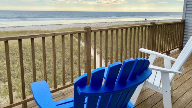 Une terrasse en bois avec deux fauteuils Adirondack donnant sur une plage.