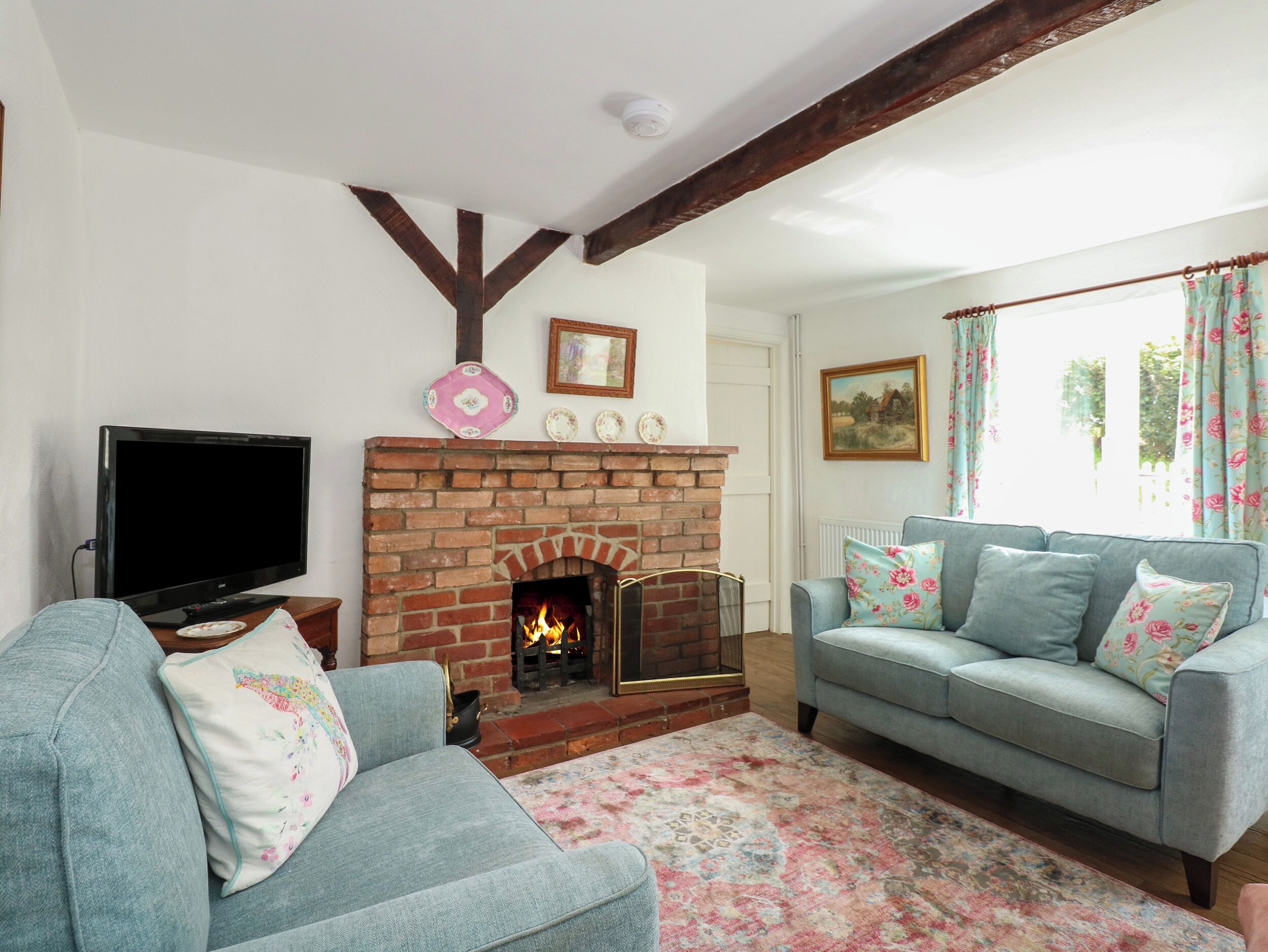 A living room with a brick fireplace, two sofas, a television, and a patterned rug.