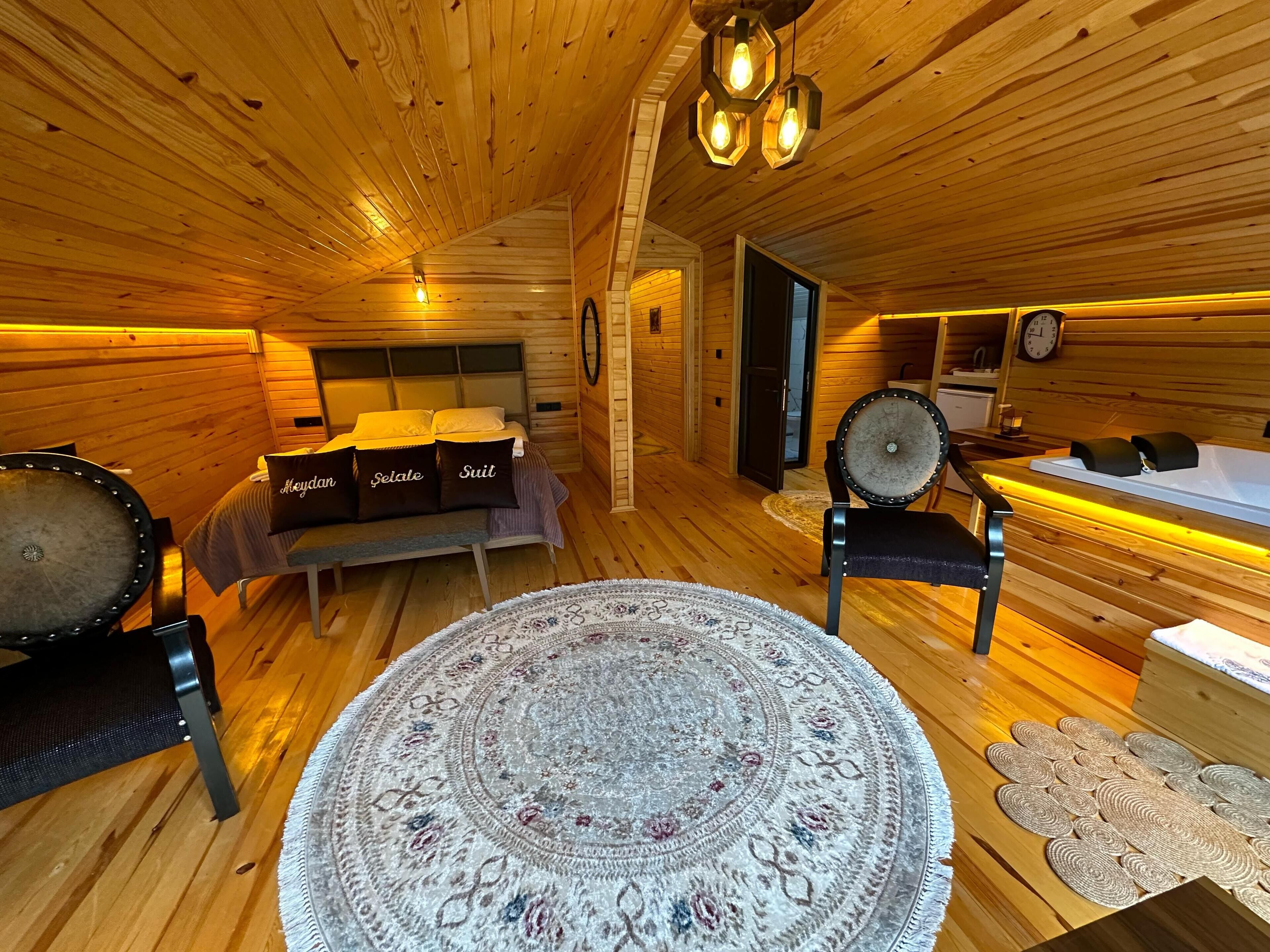 A cozy wooden cabin interior with a bed, a round rug, a chair, and a bathtub.