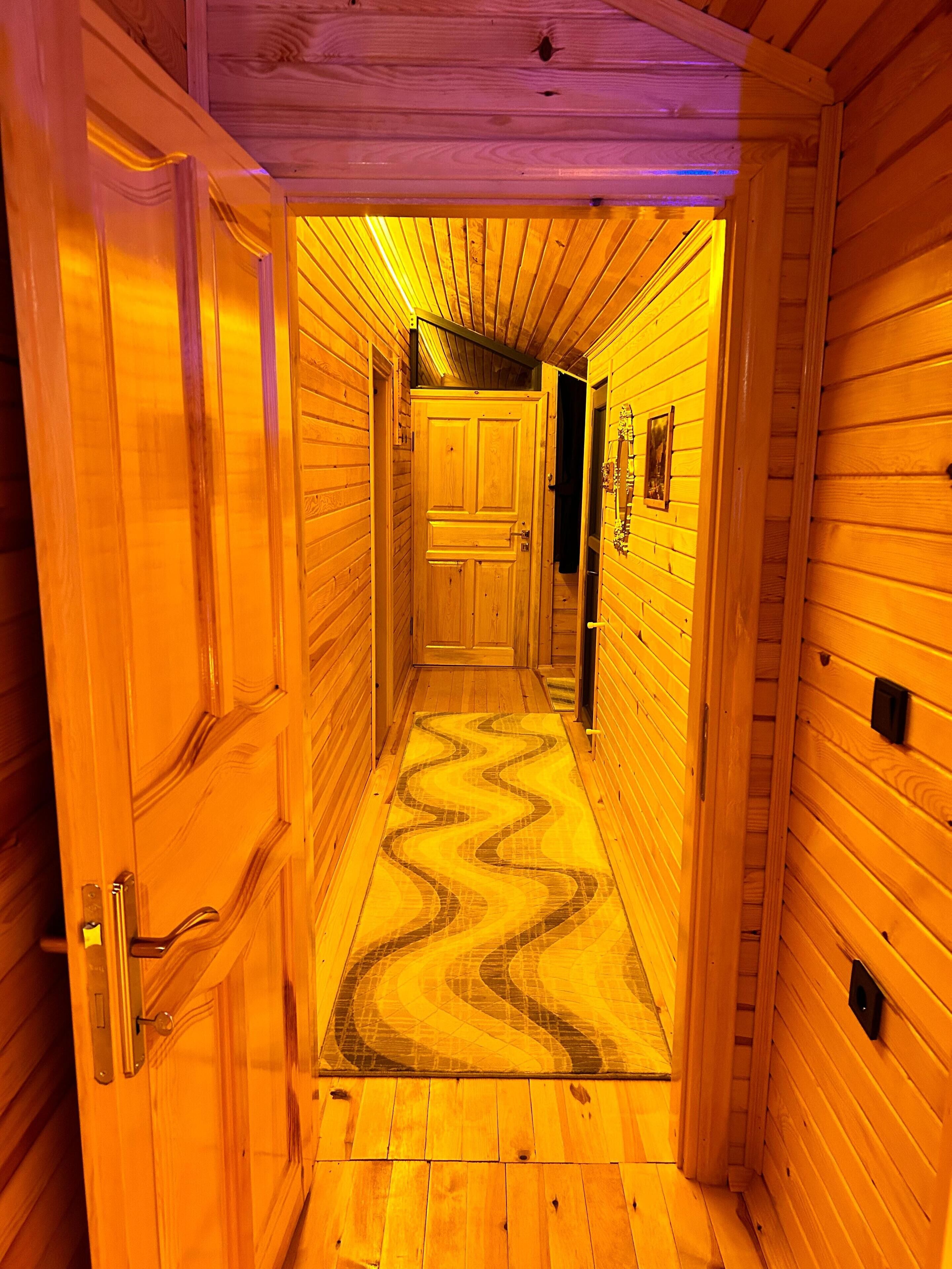 A wooden hallway with a chevron-patterned floor, wooden walls, and a door at the end.
