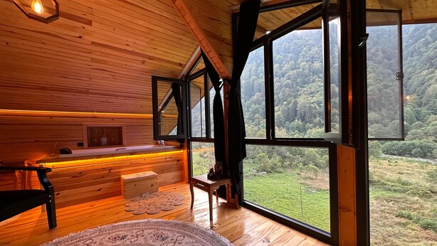Una cabaña de madera con un ventanal grande, un banco de madera, una mesita y una alfombra.