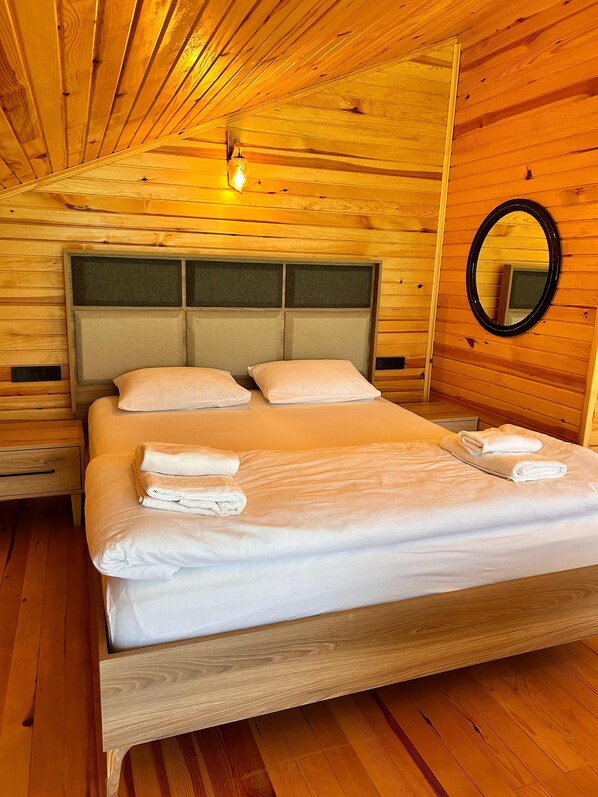 A wooden-paneled bedroom with a bed, pillows, a nightstand, a mirror, and a wall-mounted light fixture. - Meydan Şelale Dağ Evi (Çamlihemsin)
