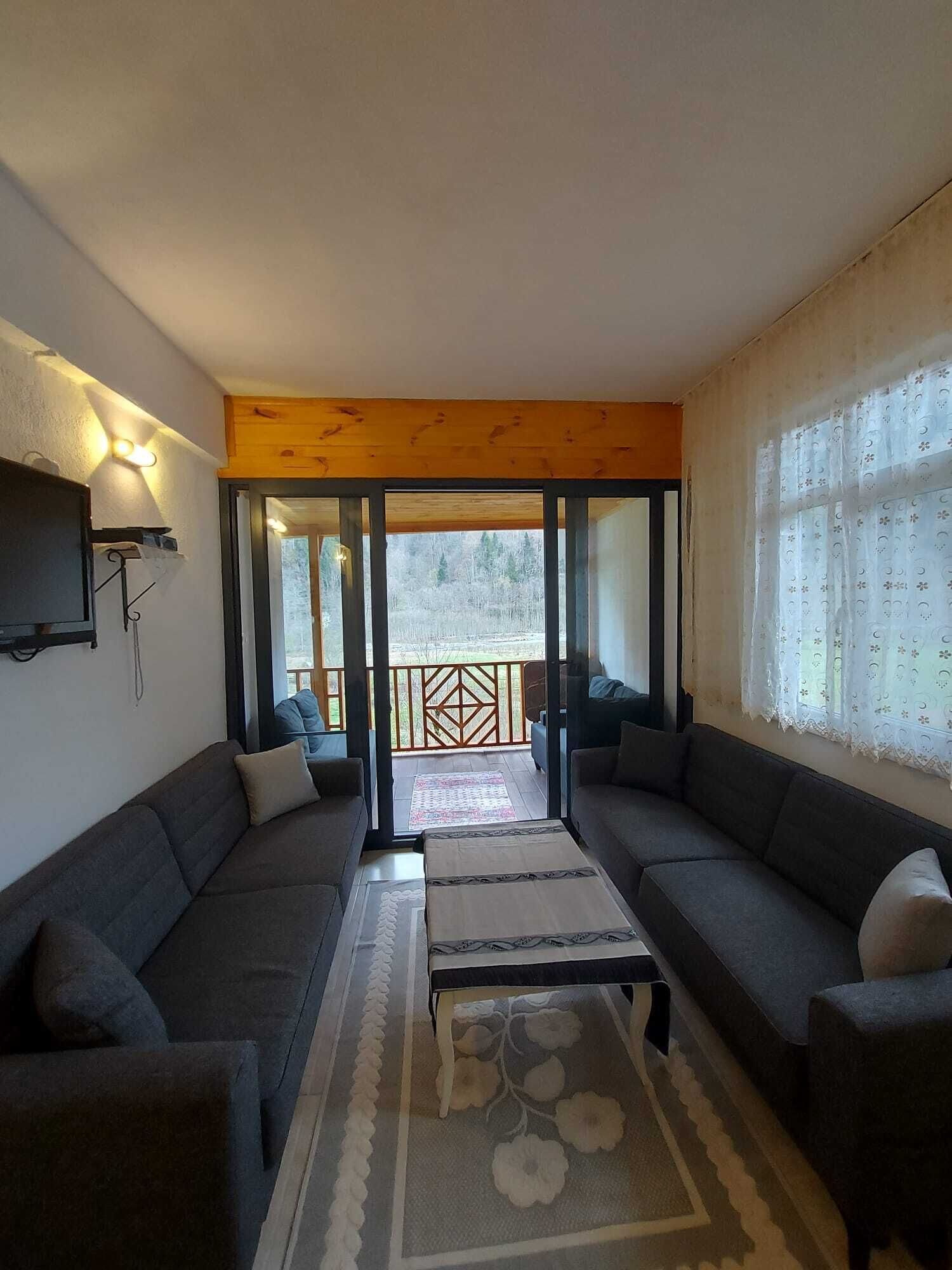 Ein Wohnzimmer mit zwei Sofas, einem Couchtisch und Blick durch eine Glastür in einen Außenbereich.