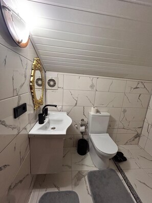 Pieni kylpyhuone, jossa on valkoinen pesuallas, wc-istuin ja kultaisella kehyksellä varustettu peili.