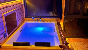Una bañera de hidromasaje de madera con ventana, velas y un banco de madera.