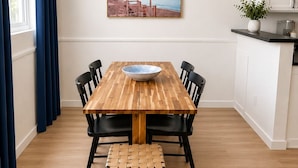 A dining area with a wooden table, black chairs, a woven bench, a bowl, and a framed picture on the wall.