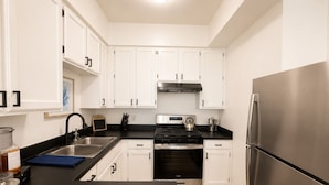 A modern kitchen with white cabinets, a stainless steel refrigerator, a gas stove, and a built-in oven.