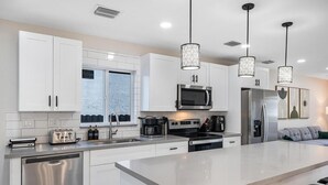 Una cocina moderna con armarios blancos, electrodomésticos de acero inoxidable e iluminación colgante.