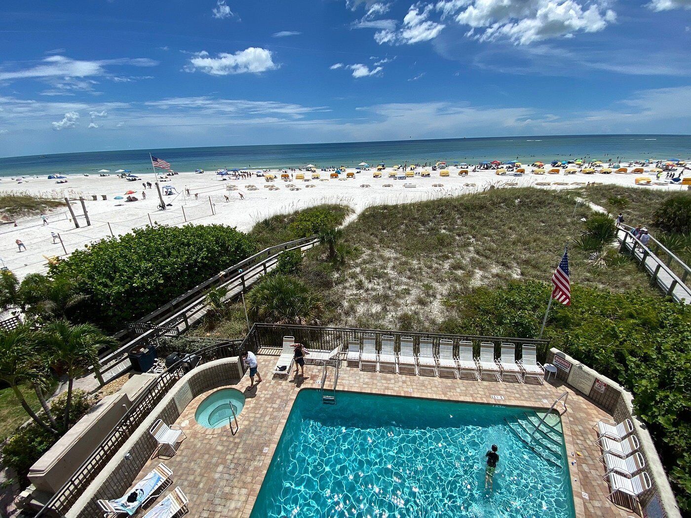 Un espace piscine avec vue sur la plage, comprenant une piscine, des chaises longues et un drapeau.