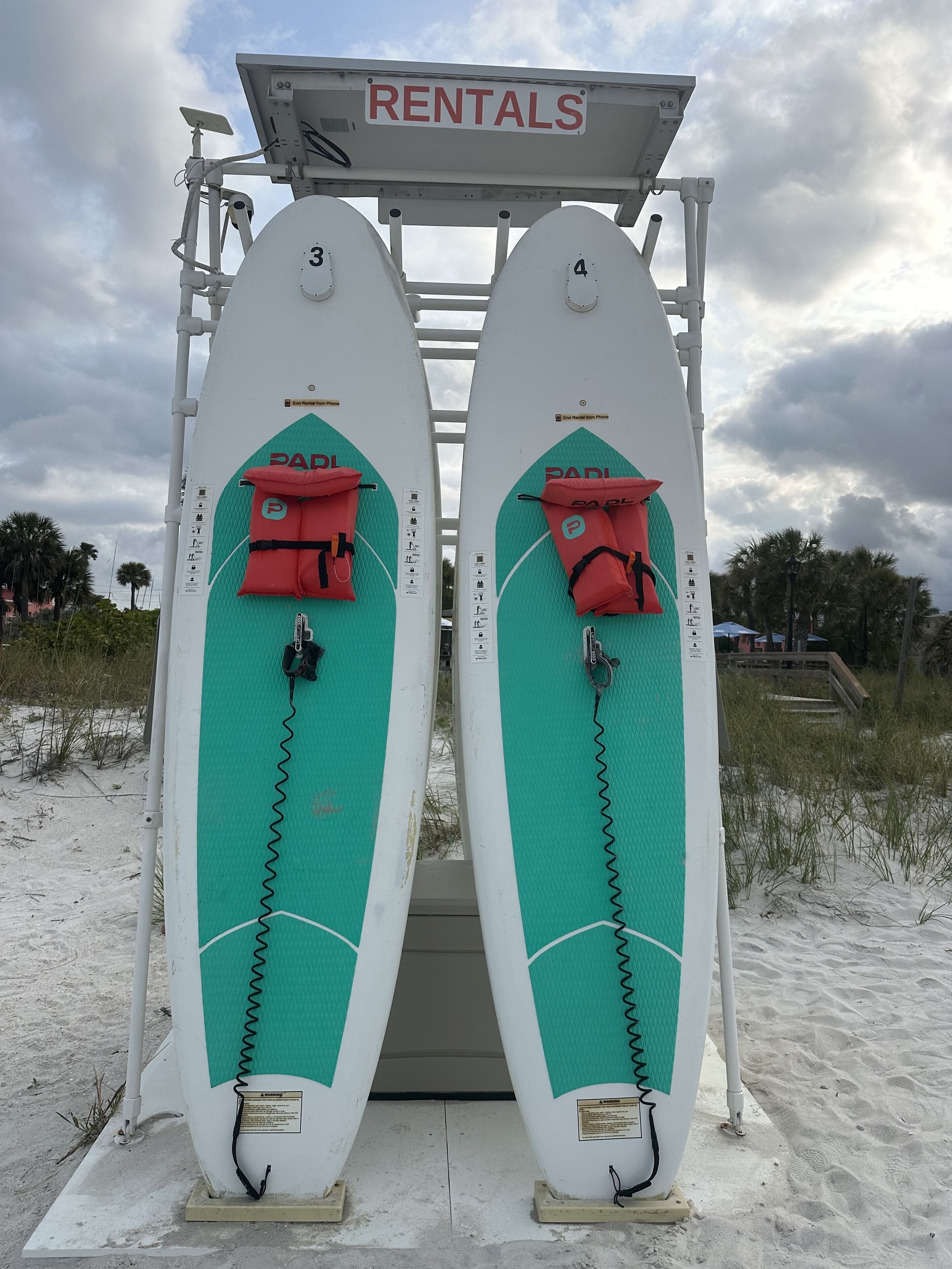 En redningsplatform med to surfboards, et skilt med 'RENTALS' og et 'PADI' logo.