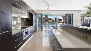 A modern kitchen with dark cabinetry, stainless steel appliances, and a large island. - Zen Bayview Bliss: Luxury Marina Mansion (Bayview)