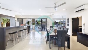 A spacious kitchen with a central island, bar stools, and a dining area with a table and chairs. - Zen Bayview Bliss: Luxury Marina Mansion (Bayview)