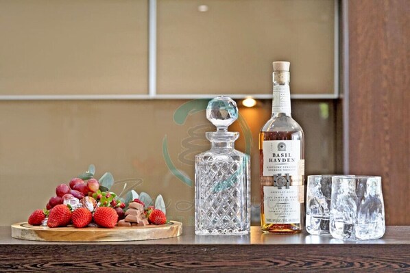 Una mesa de madera con una botella de whiskey Basil Bayden, un decantador de cristal y un plato de fresas y uvas.