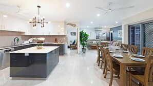 A modern kitchen with a central island, dining area with wooden chairs, and a ceiling fan. - Zenhouse Stylish: Lawn ~ Workspace ~ OutdoorDining (Muirhead)