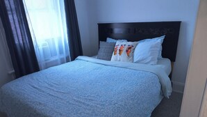 Un letto rifatto con cura, con una coperta a fantasia, una testiera scura e numerosi cuscini.
