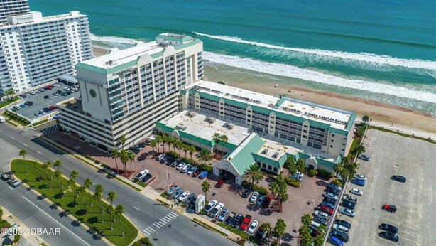 Ein Hotel mit Blick auf den Strand, mehreren Parkplätzen und einem großen Gebäude mit Gründach.