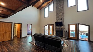 A spacious living room with a stone fireplace, wooden beams, and large windows. - Windrock Cabin On The Hill (oak ridge)