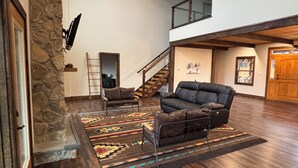 A spacious living area with a stone accent wall, a large leather sofa, and a patterned rug. - Windrock Cabin On The Hill (oak ridge)