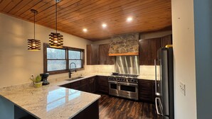 A modern kitchen with a large island, dark wood cabinets, stainless steel appliances, and a stone accent wall. - Windrock Cabin On The Hill (oak ridge)