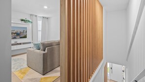 A modern living room with a grey sofa, a flat-screen TV, and a wooden slatted partition. - Bright 3BR Townhouse w/ Loft, Near Disney, Pool & Gym Access (Kissimmee)