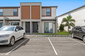Un bâtiment moderne avec un parking, deux voitures garées devant et un petit arbre.