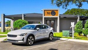 A white car parked at an electric vehicle charging station in front of a building with a sign reading "The Hub." - Bright 3BR Townhouse w/ Loft, Near Disney, Pool & Gym Access (Kissimmee)