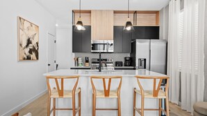 A modern kitchen with a central island, bar stools, and pendant lighting. - Bright 3BR Townhouse w/ Loft, Near Disney, Pool & Gym Access (Kissimmee)