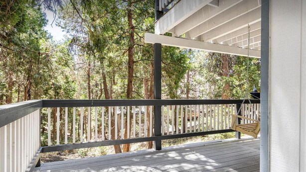 Una terraza de madera con barandilla blanca, rodeada de árboles altos.