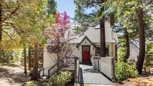 A house with a red door, surrounded by trees and a wooden deck leading to the entrance. - Arrowhead cabin sleeps 12 fast wifi newly remodeled (Lake Arrowhead)