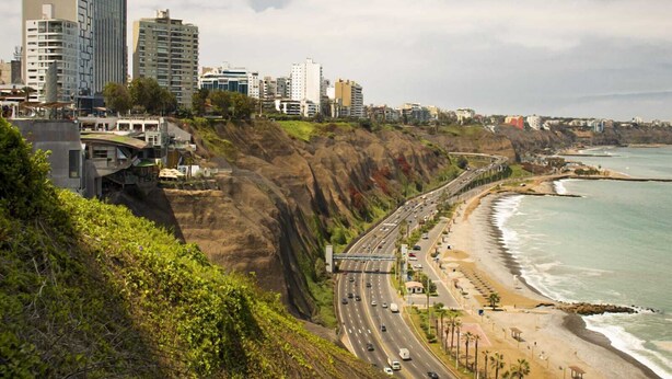 Un paysage urbain côtier avec une autoroute longeant la plage, des immeubles de grande hauteur et une falaise.