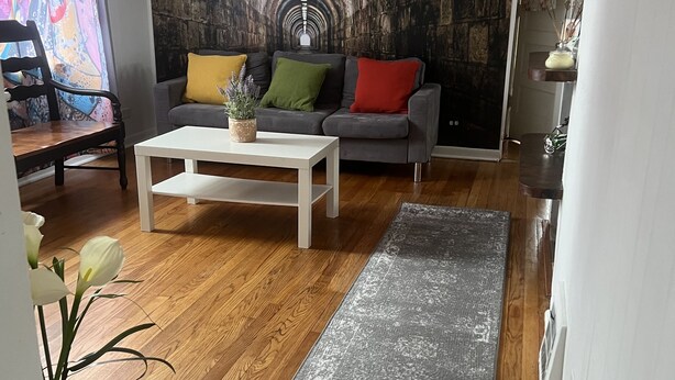Een woonkamer met een grijze bank, een witte salontafel en een grijs vloerkleed.