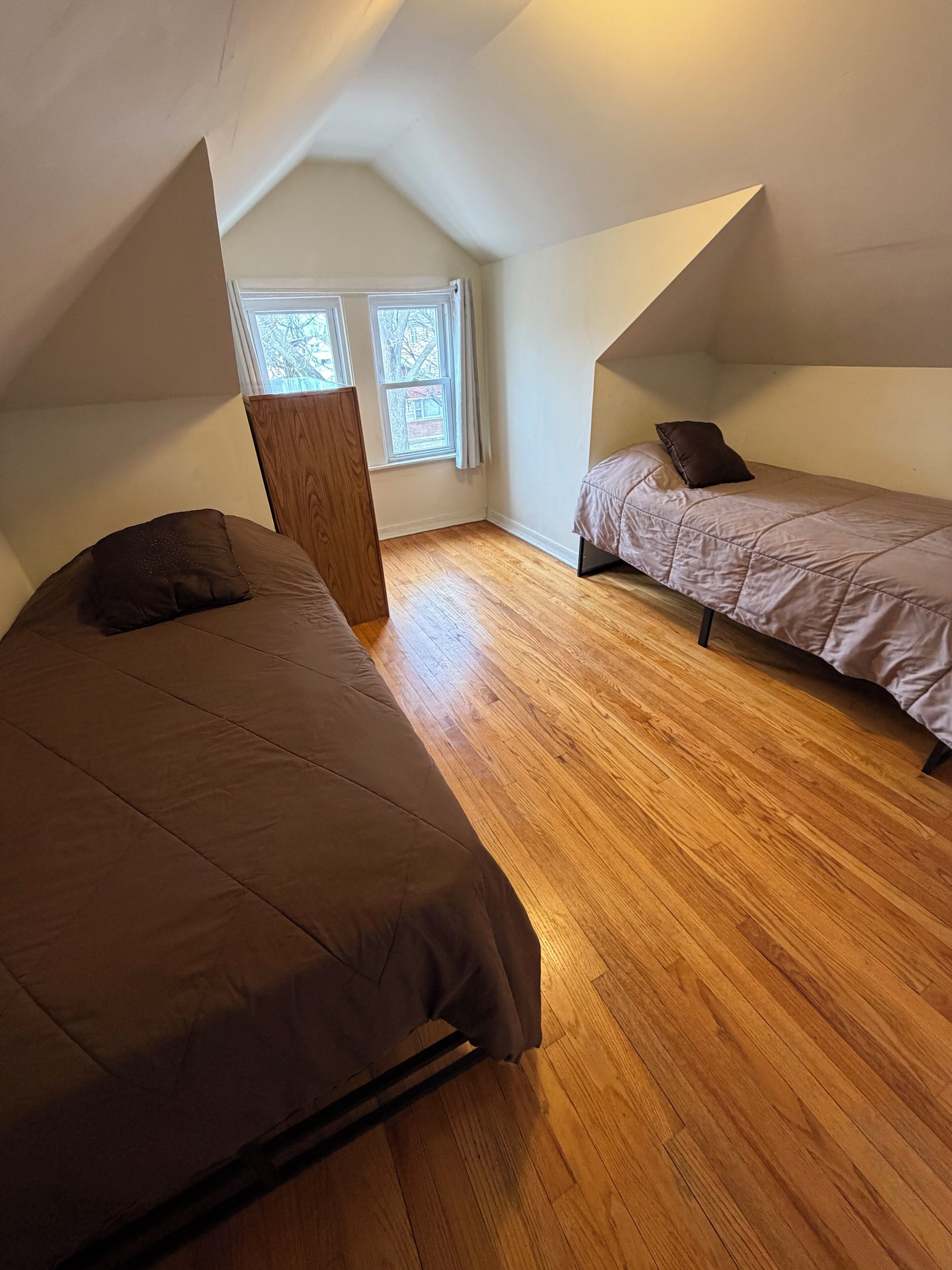 Una habitación pequeña y acogedora con dos camas, suelo de madera y techo inclinado.