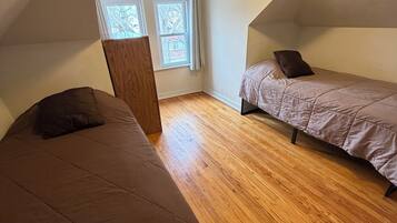 Una habitación pequeña y acogedora con dos camas, suelo de madera y techo inclinado.
