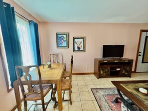 Een eetruimte met een houten tafel en stoelen, een televisie op een kast, en twee ingelijste kunstwerken aan de muur.