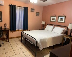 A bedroom with a bed, two bedside tables, a desk, a chair, a window with curtains, and a ceiling fan. - Peek-a-Moo Apt w/patio, paddle boating (Raymondville)