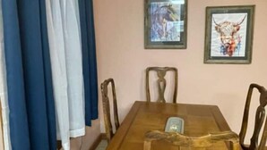 A dining area with a wooden table, chairs, and curtains. There are two framed pictures on the wall. - Peek-a-Moo Apt w/patio, paddle boating (Raymondville)